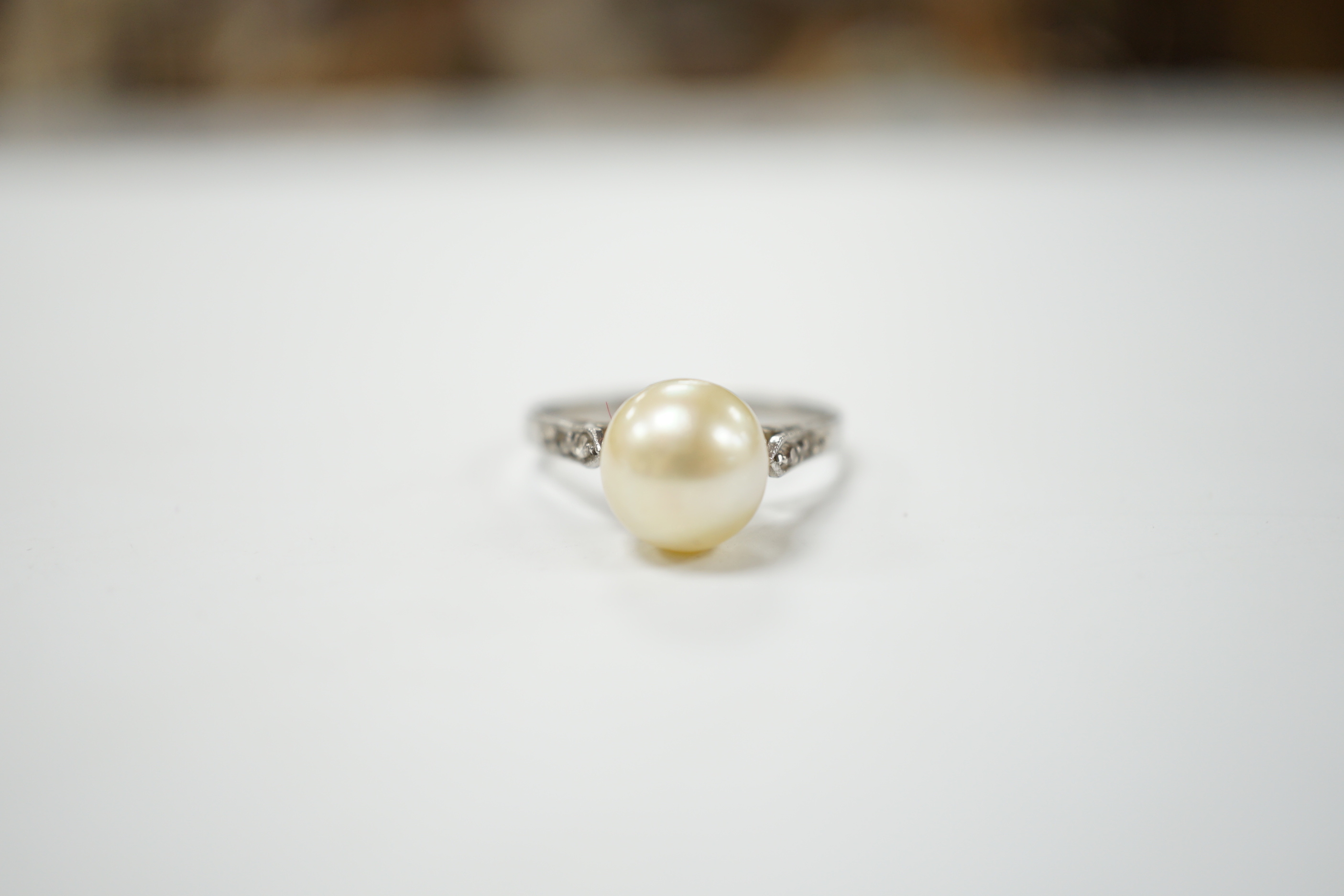 A white metal solitaire cultured pearl ring with diamond set shoulders, size J